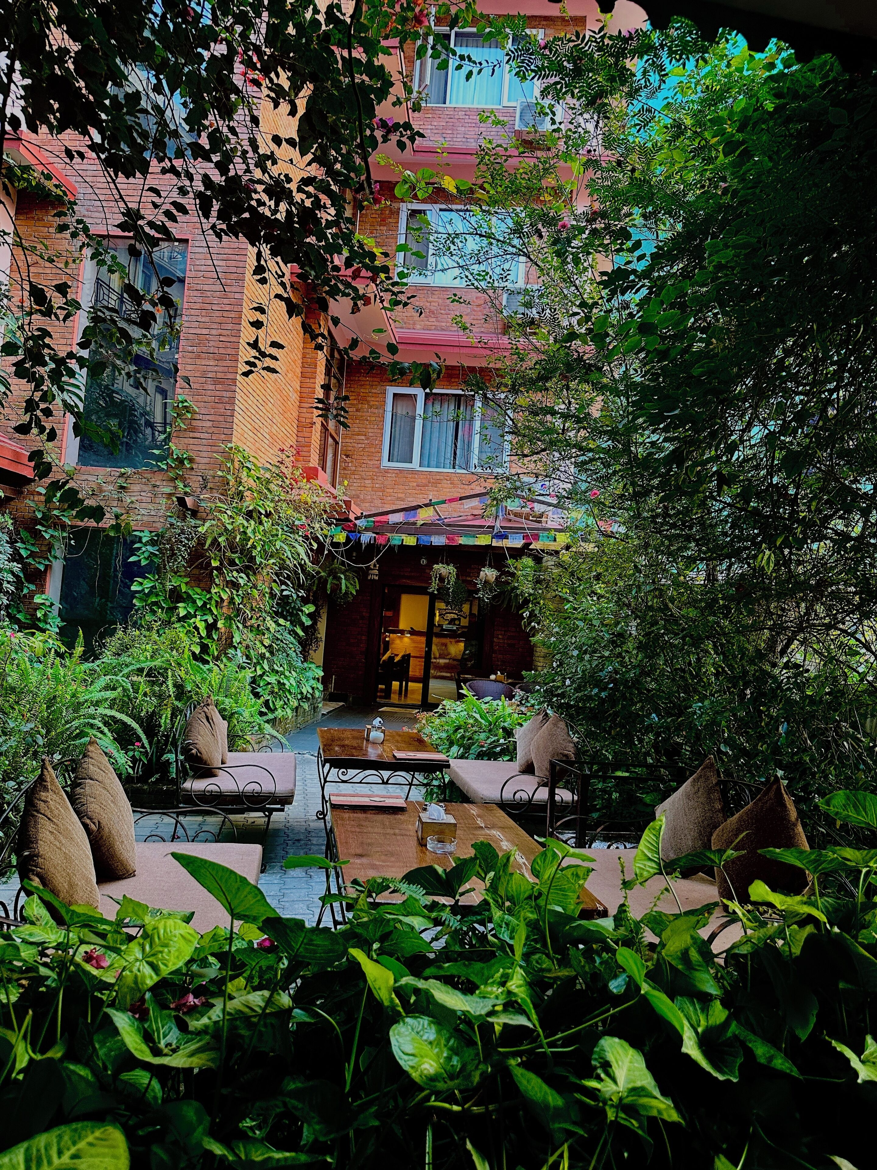 A courtyard with a brick building, outdoor seating, and lush greenery.