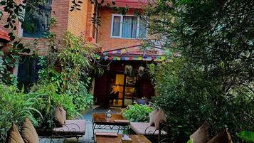 Un patio con un edificio de ladrillo, mobiliario exterior y abundante vegetación.