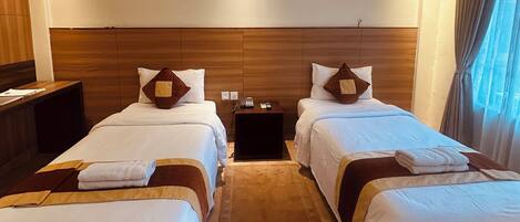 Una habitación de hotel con dos camas, un ventilador de techo, una mesita de noche y una ventana con cortinas.
