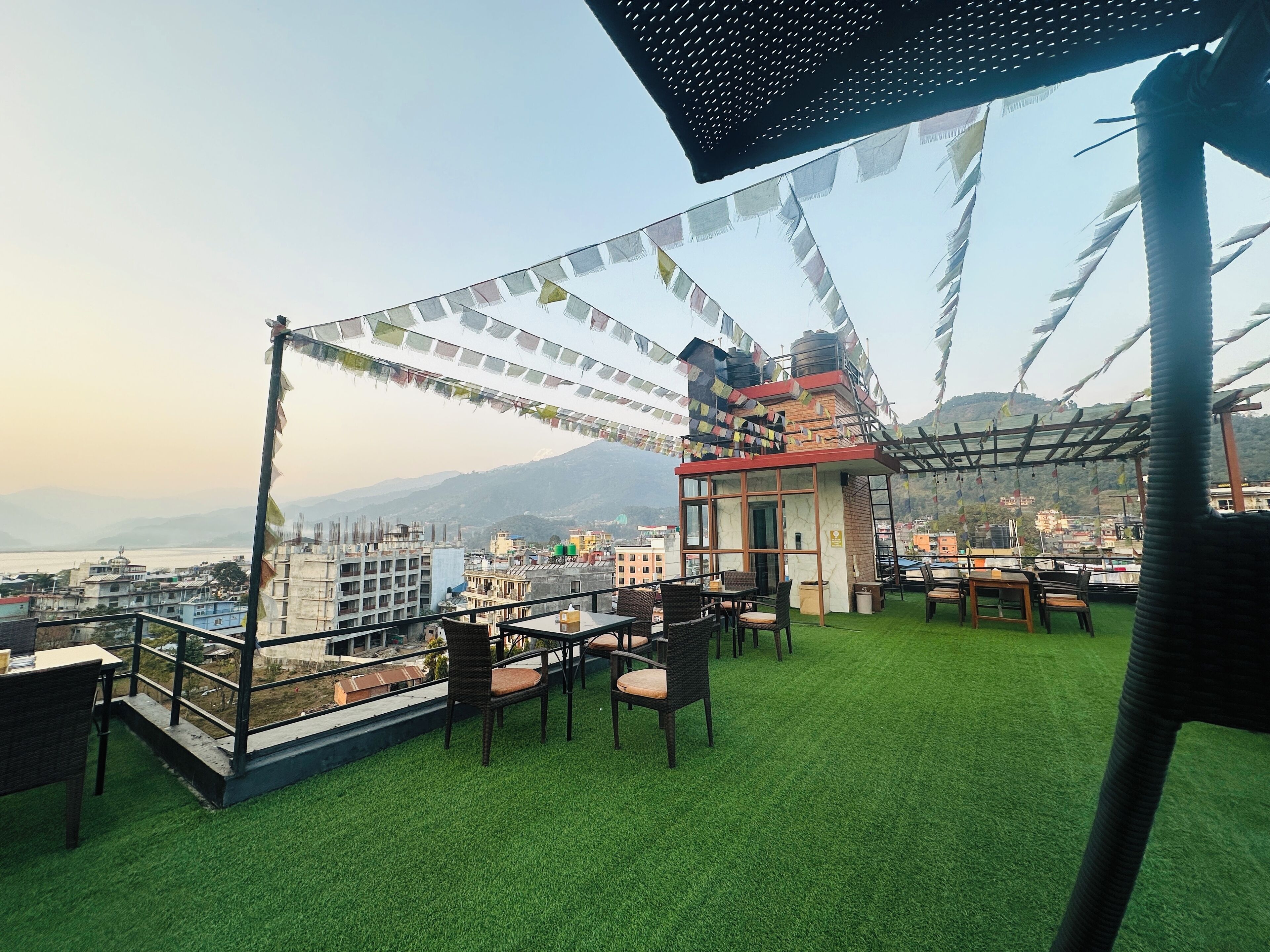 A rooftop terrace with artificial grass, outdoor seating, and a view of the city and mountains.