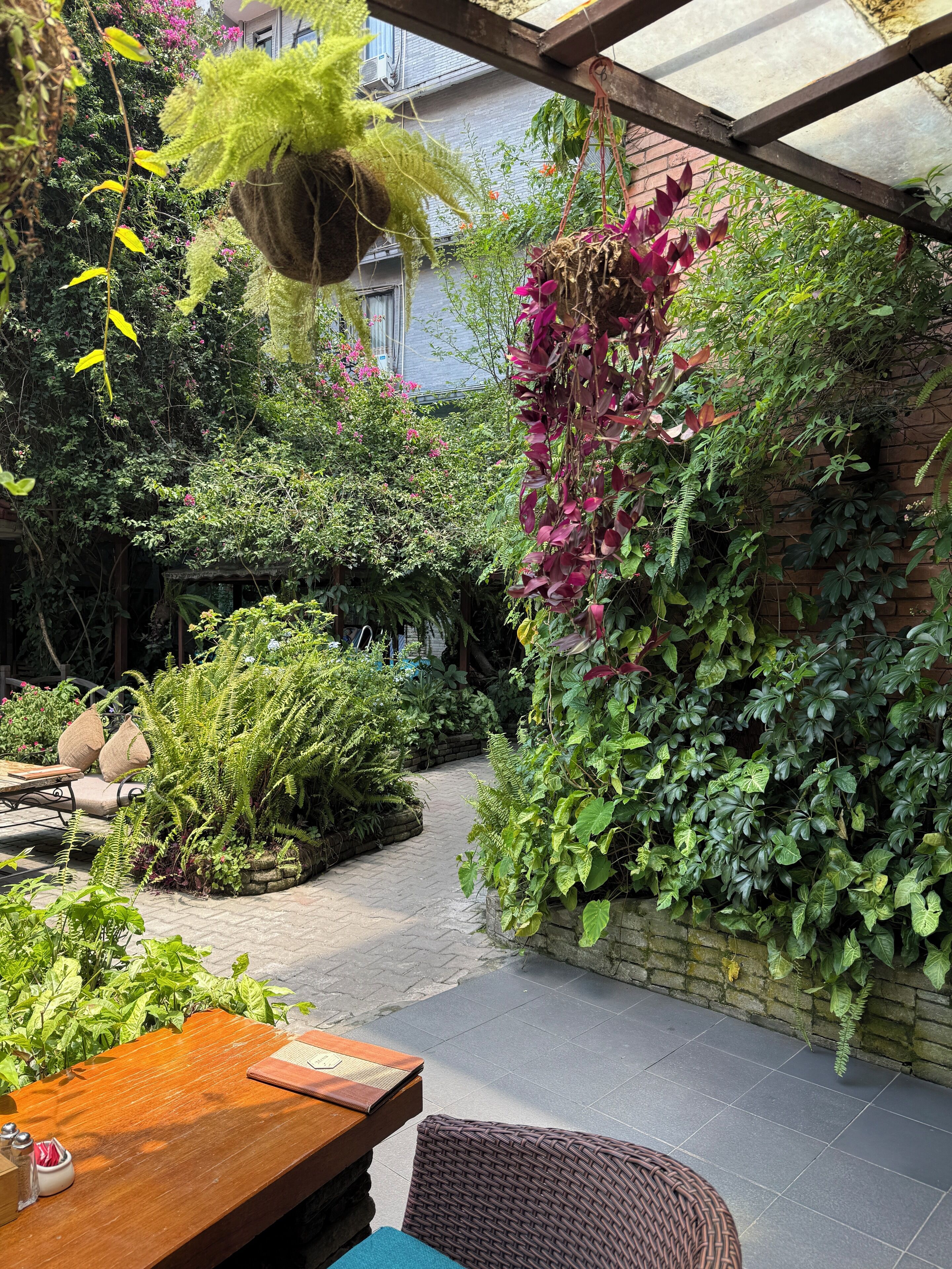 Un patio jardín con mesa de madera, sillas de mimbre y plantas diversas.