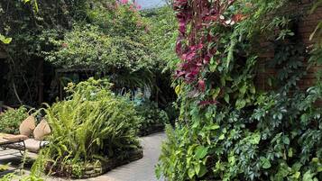 Un patio jardín con mesa de madera, sillas de mimbre y plantas diversas.