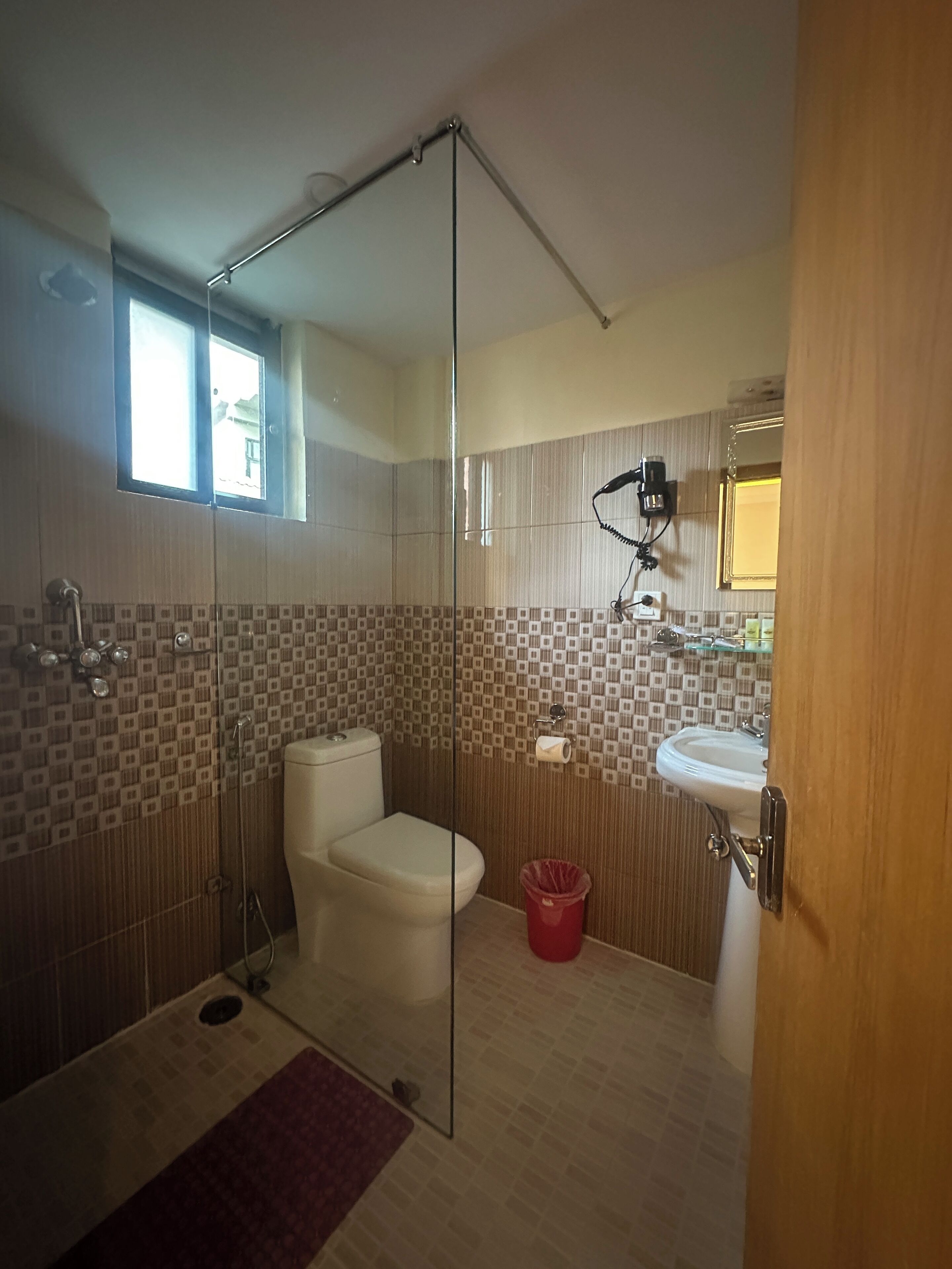 A modern bathroom with a glass shower enclosure, a toilet, a sink, and a red trash bin.