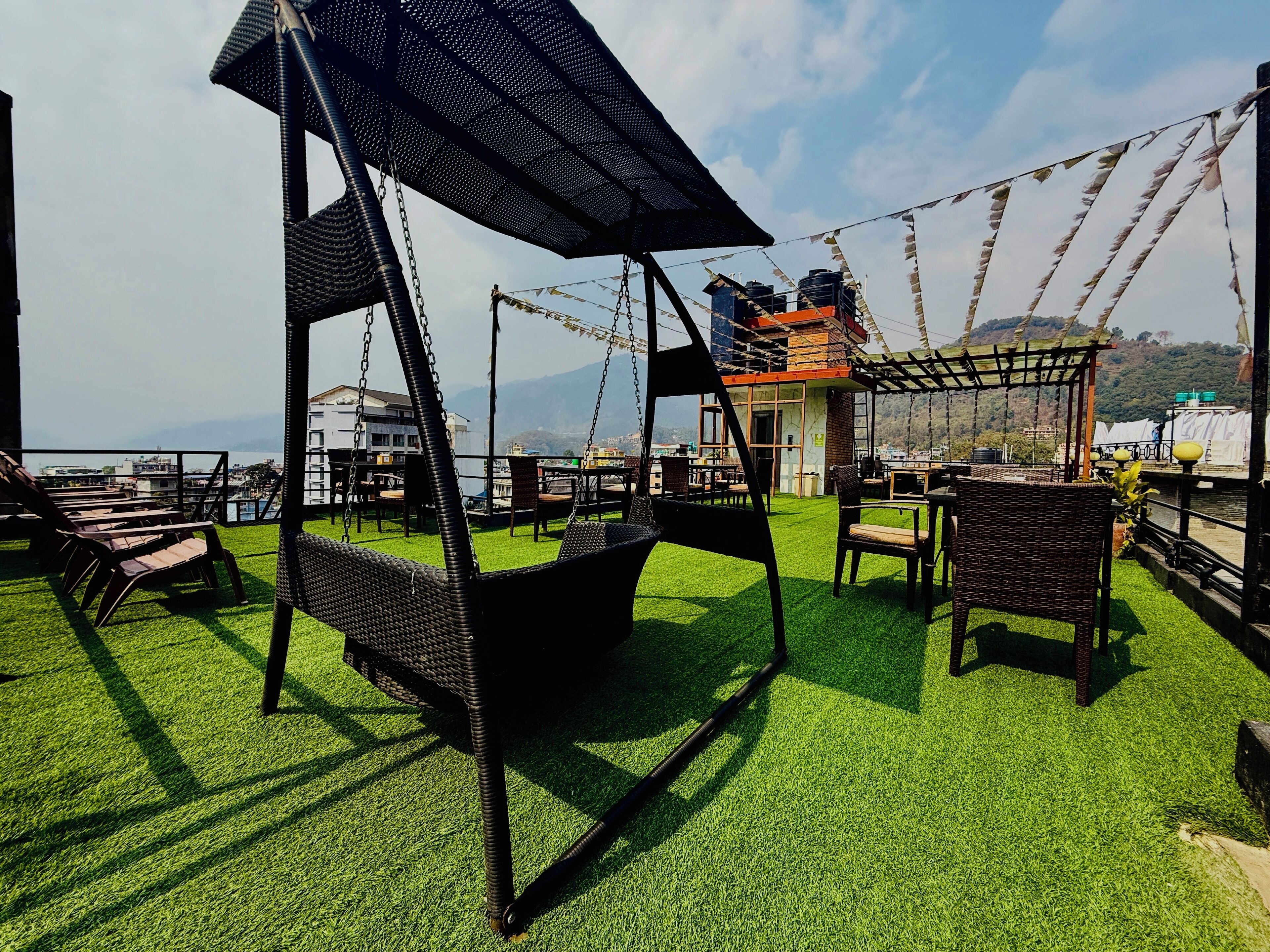 A rooftop terrace with artificial grass, wicker furniture, and a swing chair.