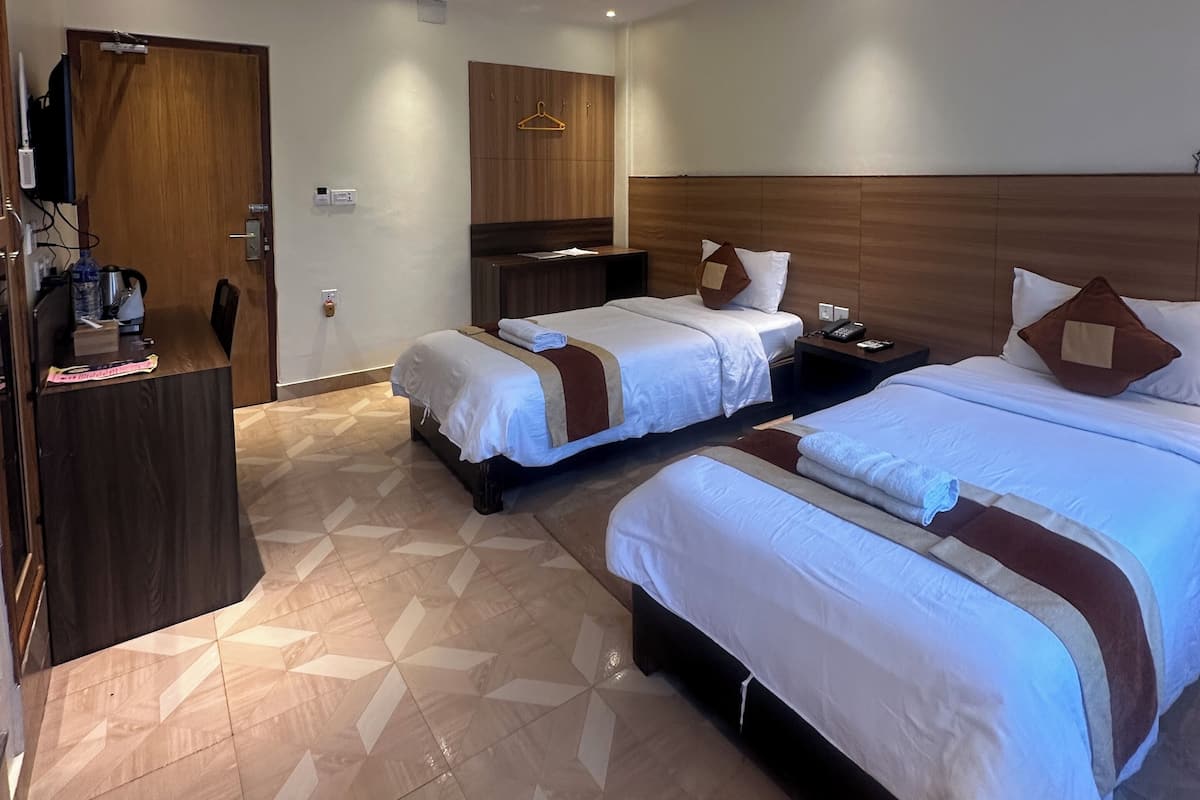 A hotel room with two beds, a desk, a wardrobe, and a ceiling fan.
