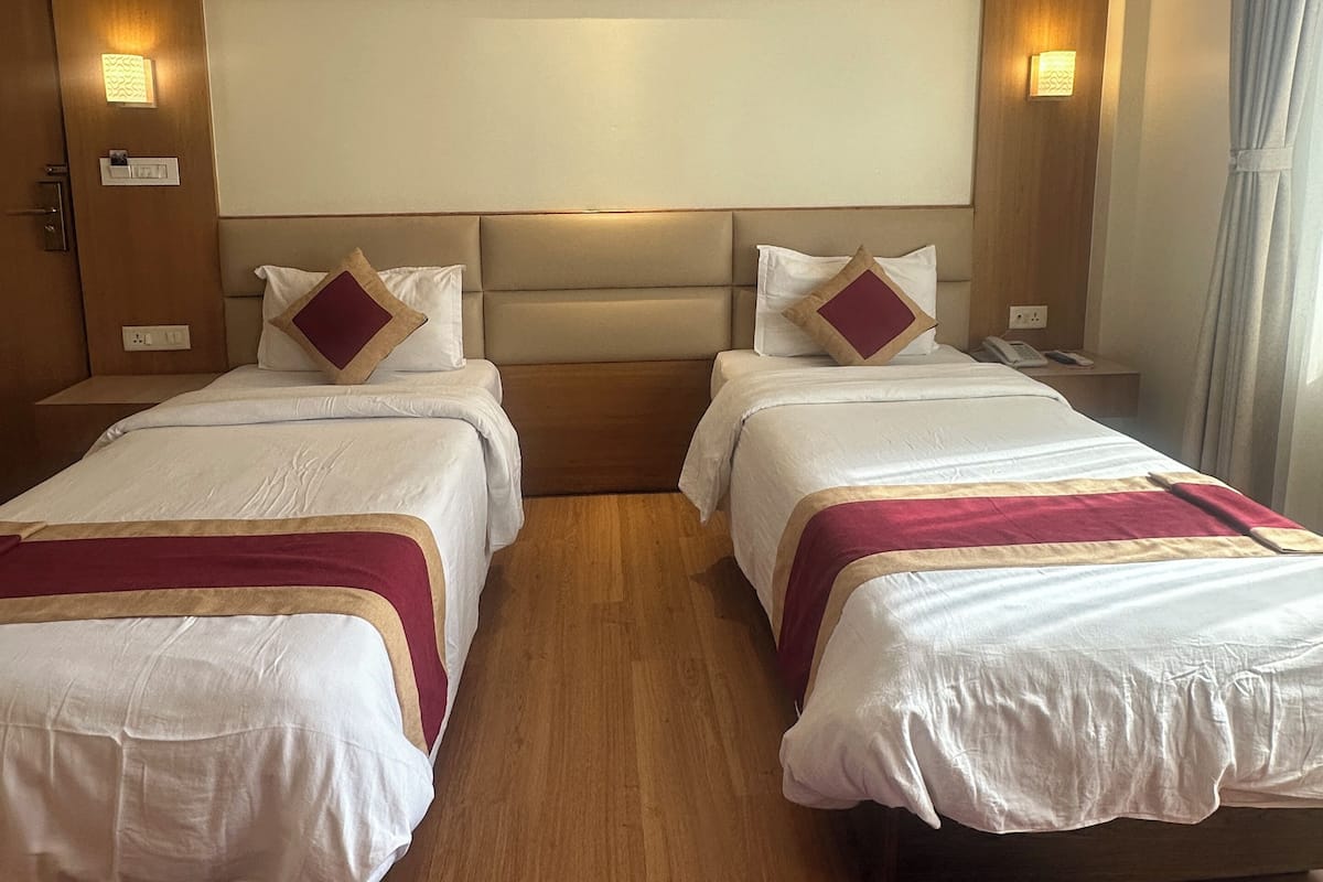 A hotel room with two beds, a wooden headboard, bedside lamps, a purple rug, and a large window with curtains.