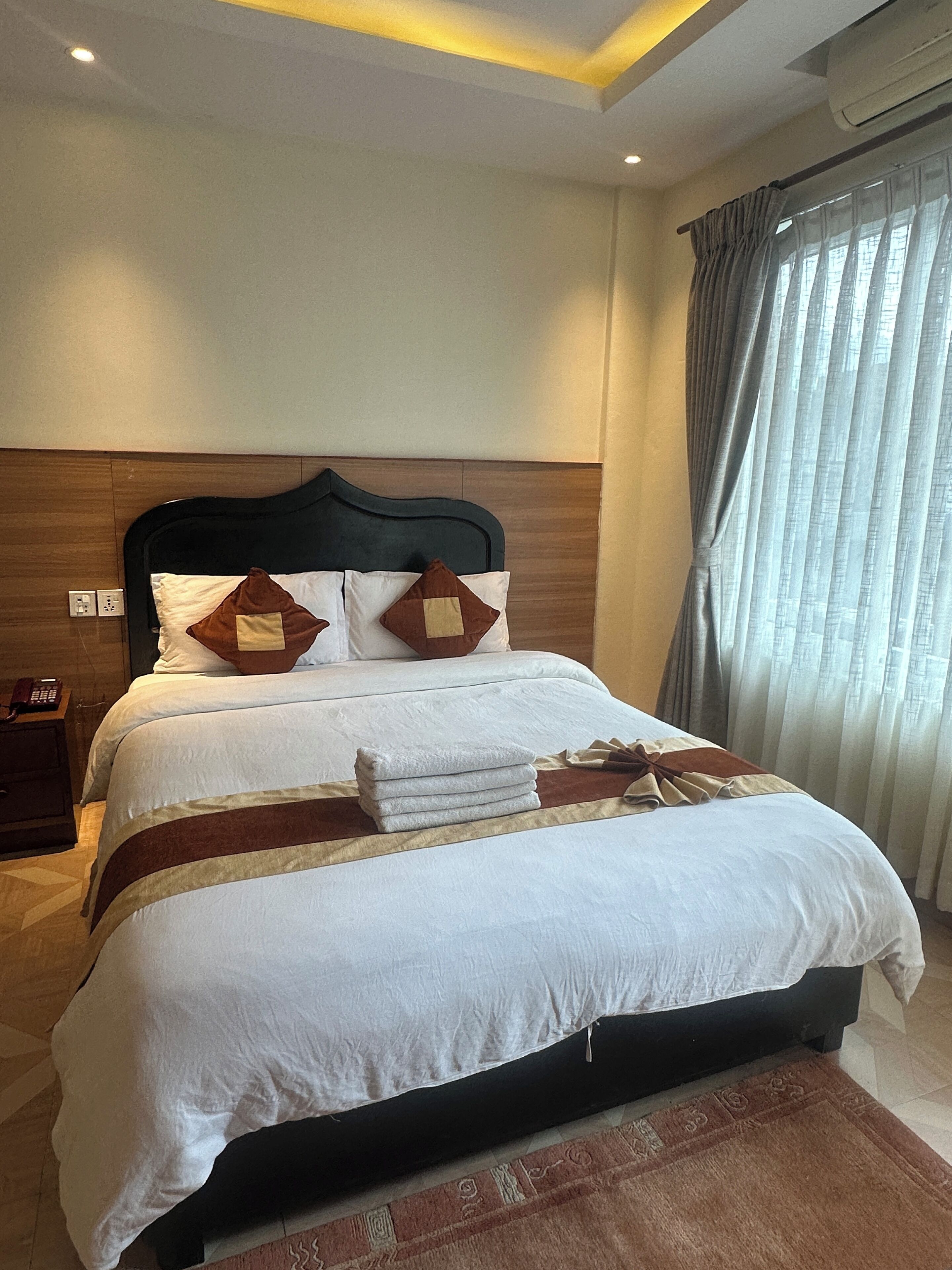 A neatly made bed with white linens, a dark headboard, and decorative pillows.