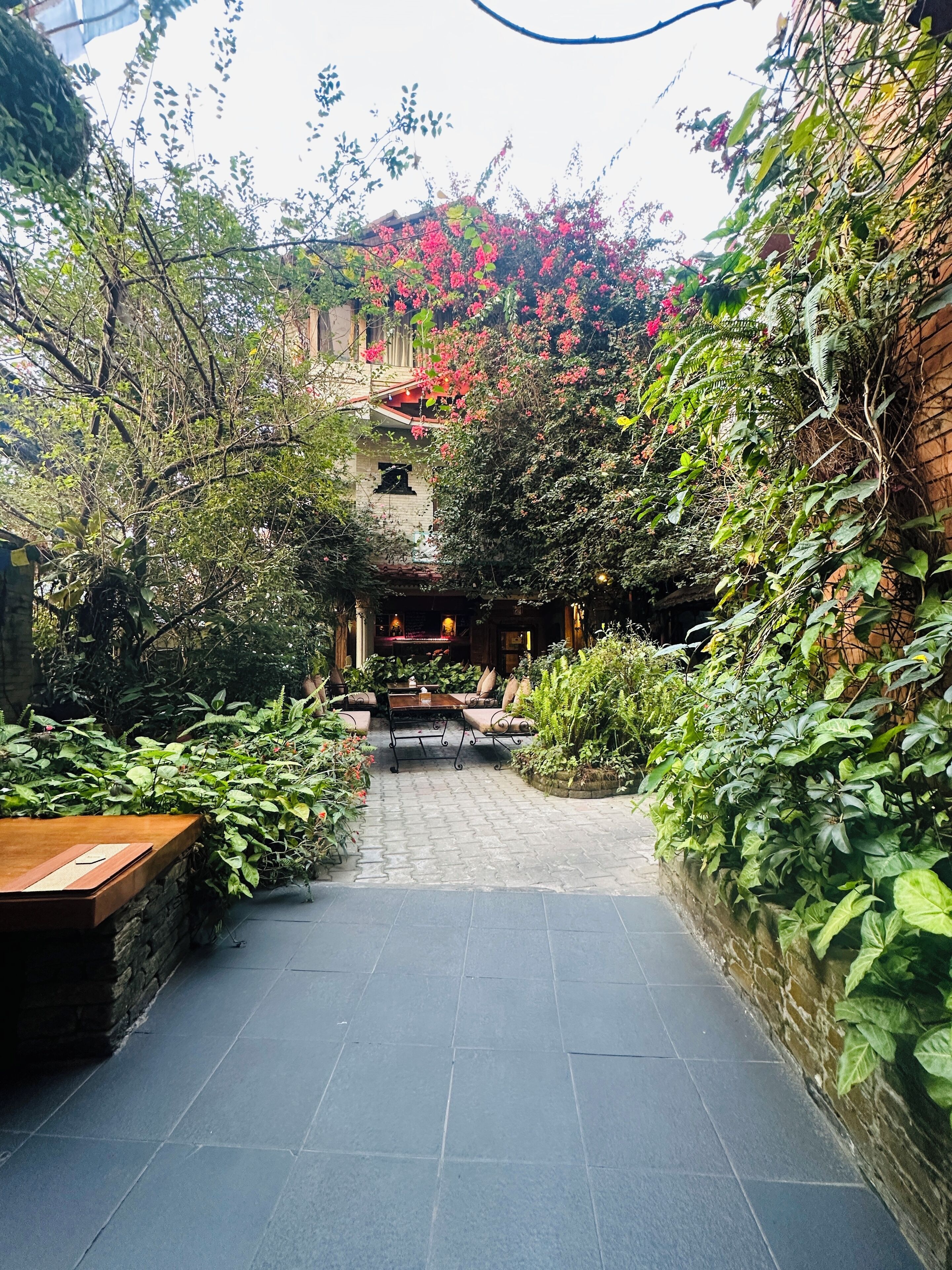 A courtyard with a paved walkway, a wooden bench, and a table.