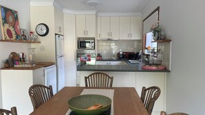 A modern kitchen with white cabinets, a microwave, oven, and a sink. There's a dining table with chairs and a green bowl on the placemat.
