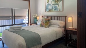 A bedroom with a bed, a nightstand, a lamp, a painting, and a window with curtains.