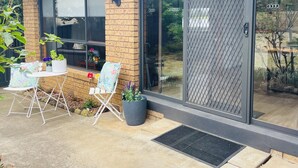 A modern house with a brick exterior, large sliding glass doors, a small patio with a table and chairs, and potted plants.
