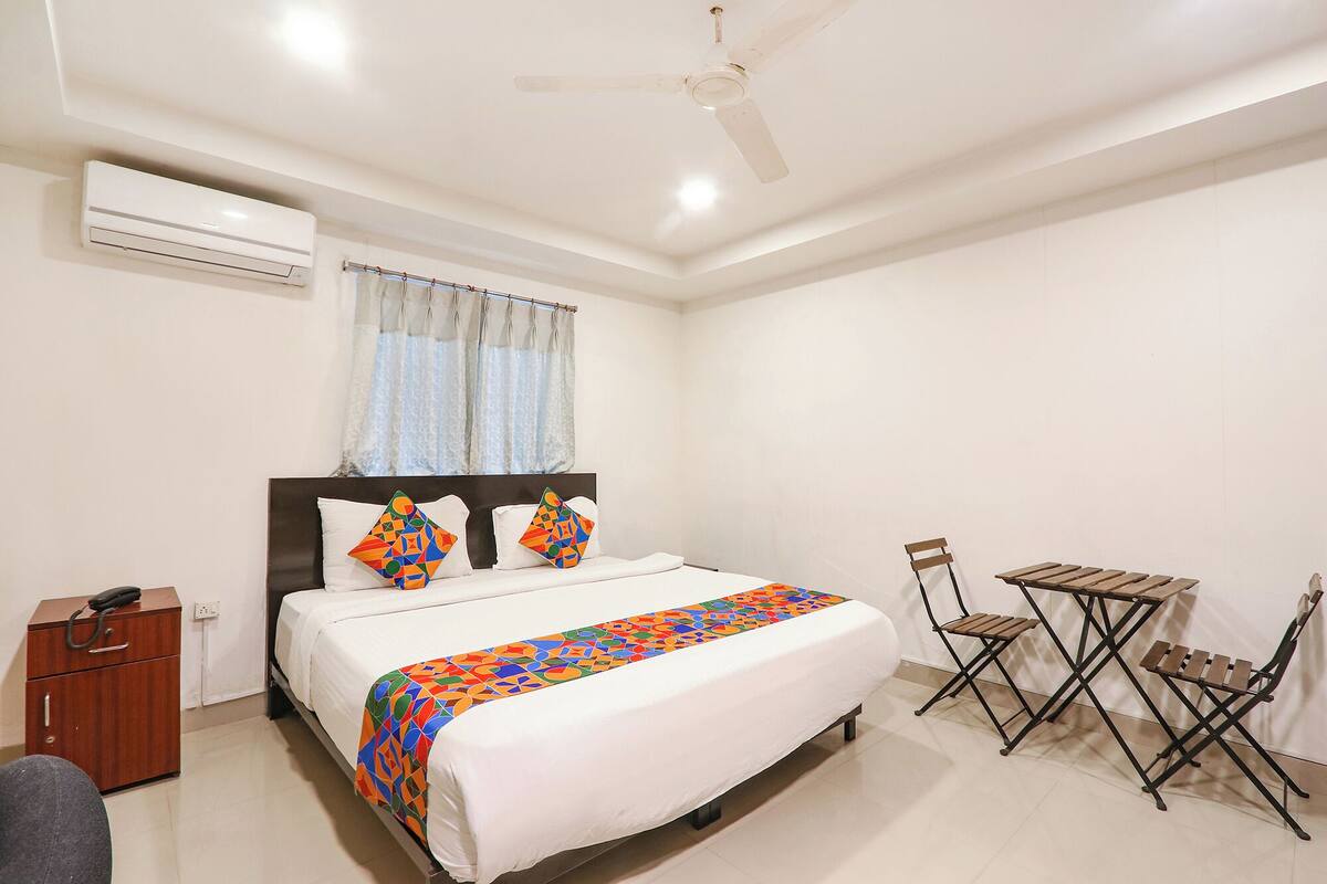 A hotel room with a bed, a desk, a chair, a small table, and a ceiling fan.