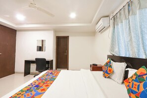 A hotel room with a bed, a desk, a chair, a mirror, and an air conditioning unit. - Hotel Blue Dawn - Near DLF Cyber City, Gachibowli (Hyderabad)