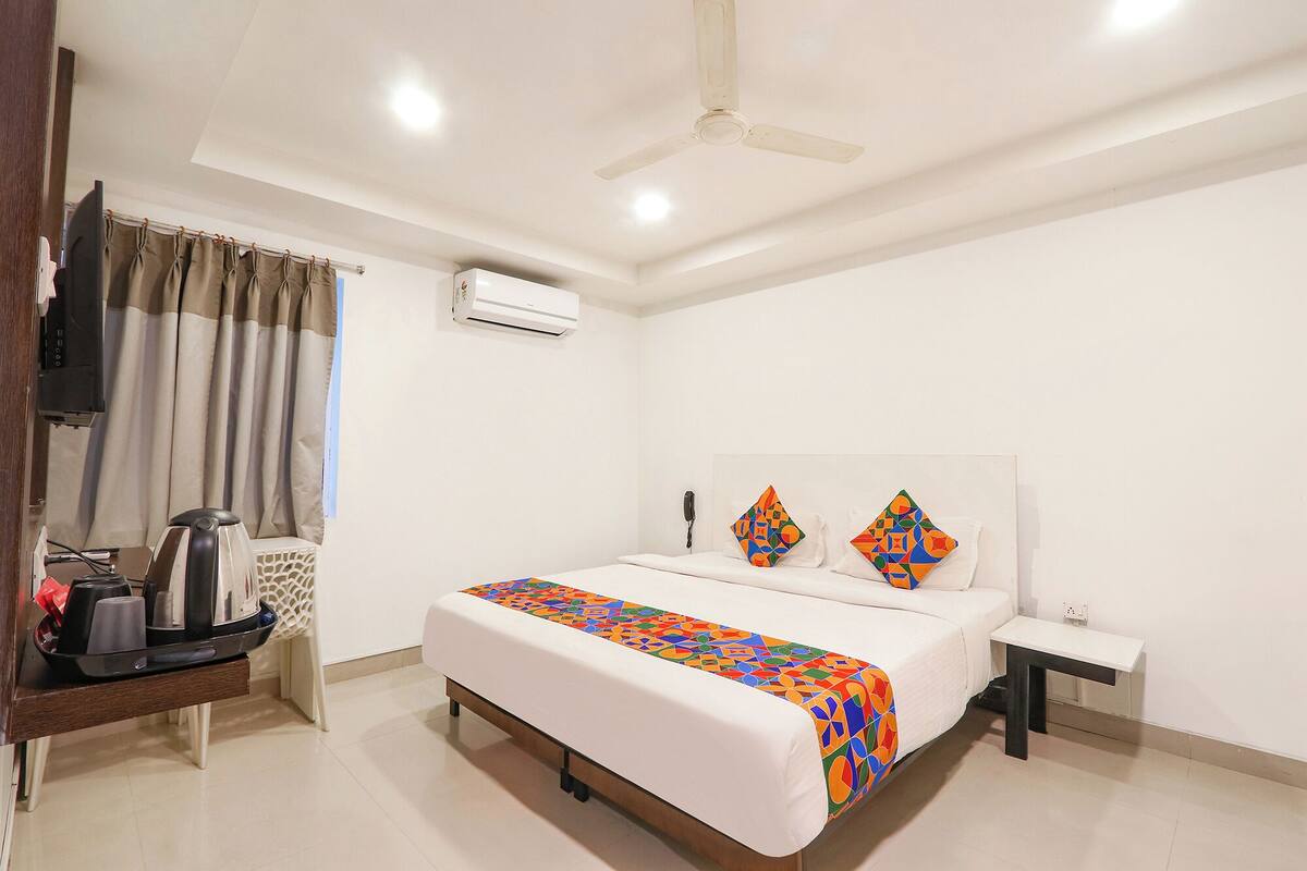 A hotel room with a bed, a bedside table, a desk with a telephone, and an air conditioning unit.