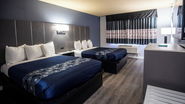 Habitación de hotel con dos camas, un escritorio y un ventanal con cortinas.