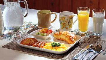 Una mesa de desayuno con un croissant, fruta, huevos revueltos y una jarra de agua.