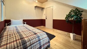 A bedroom with a bed, a wooden floor, a white door, and a potted plant.