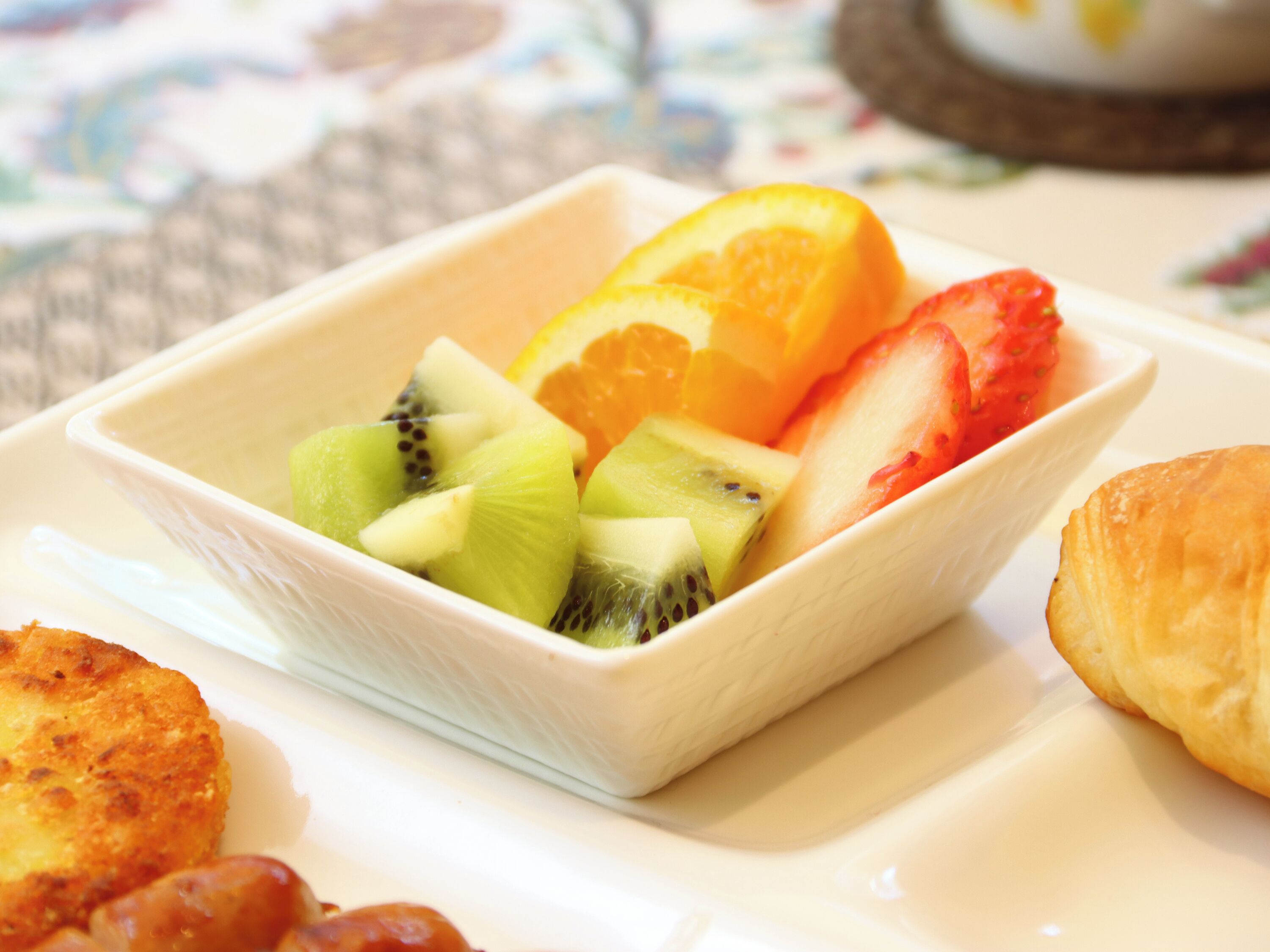 A bowl of fruit including kiwi, orange, and strawberry slices on a white plate.
