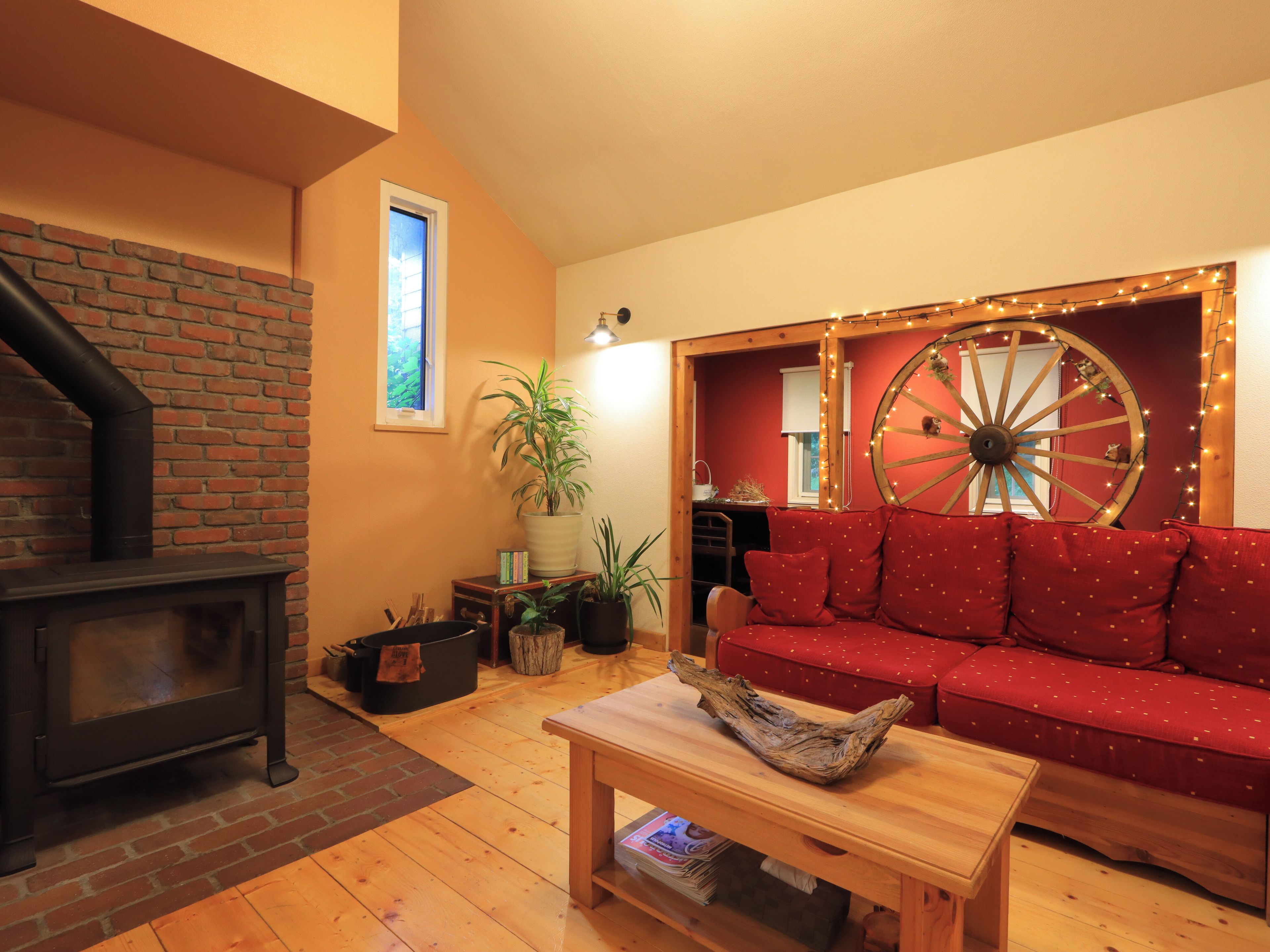 A cozy living room with a fireplace, a red sofa, a wooden table, and a decorative wheel.
