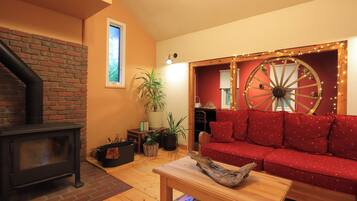 A cozy living room with a fireplace, a red sofa, a wooden table, and a decorative wheel.