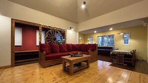 A cozy living room with a wooden floor, a red sofa, a wooden coffee table, and a large wooden wheel.