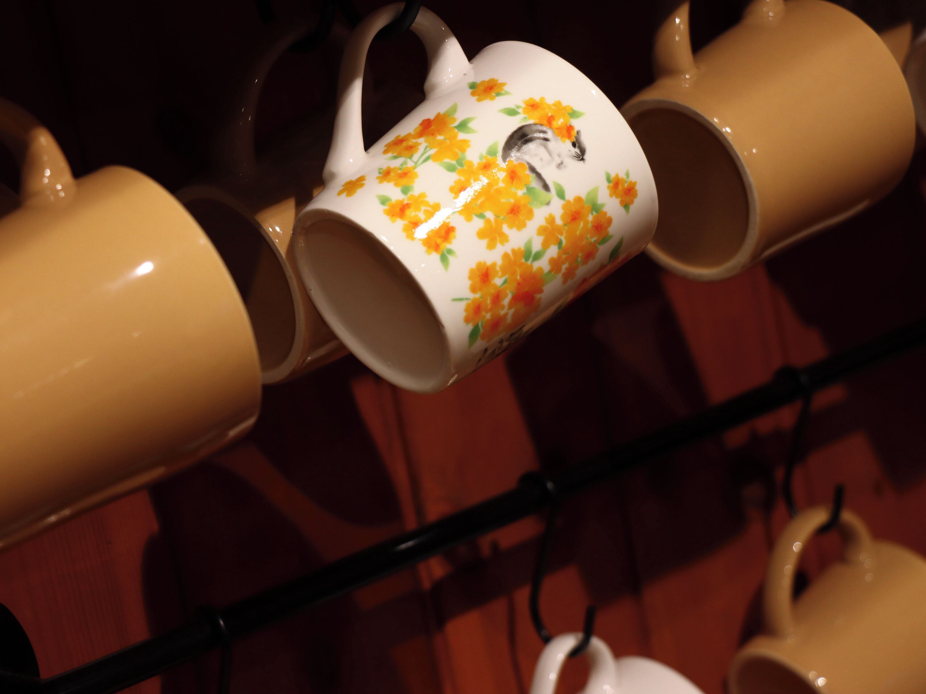 A display of ceramic mugs with floral designs and a mouse illustration, arranged on shelves.