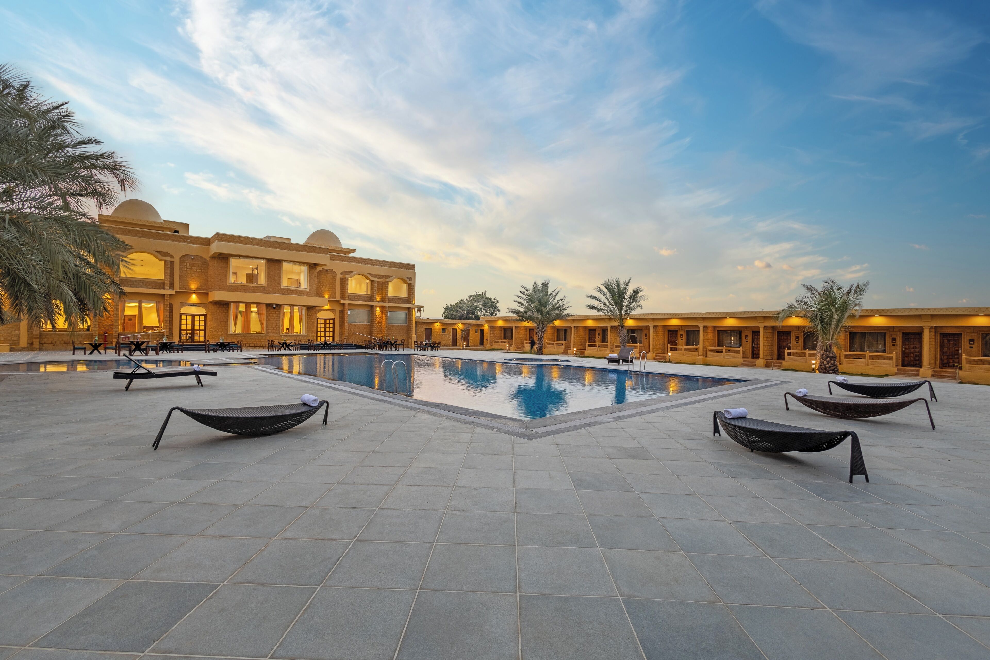 A pool area with lounge chairs and a building with multiple windows and balconies.