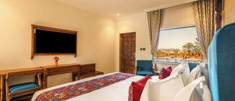 Ein Hotelzimmer mit Bett, Schreibtisch, Stuhl, Fernseher und Fenster mit Blick auf Palmen.