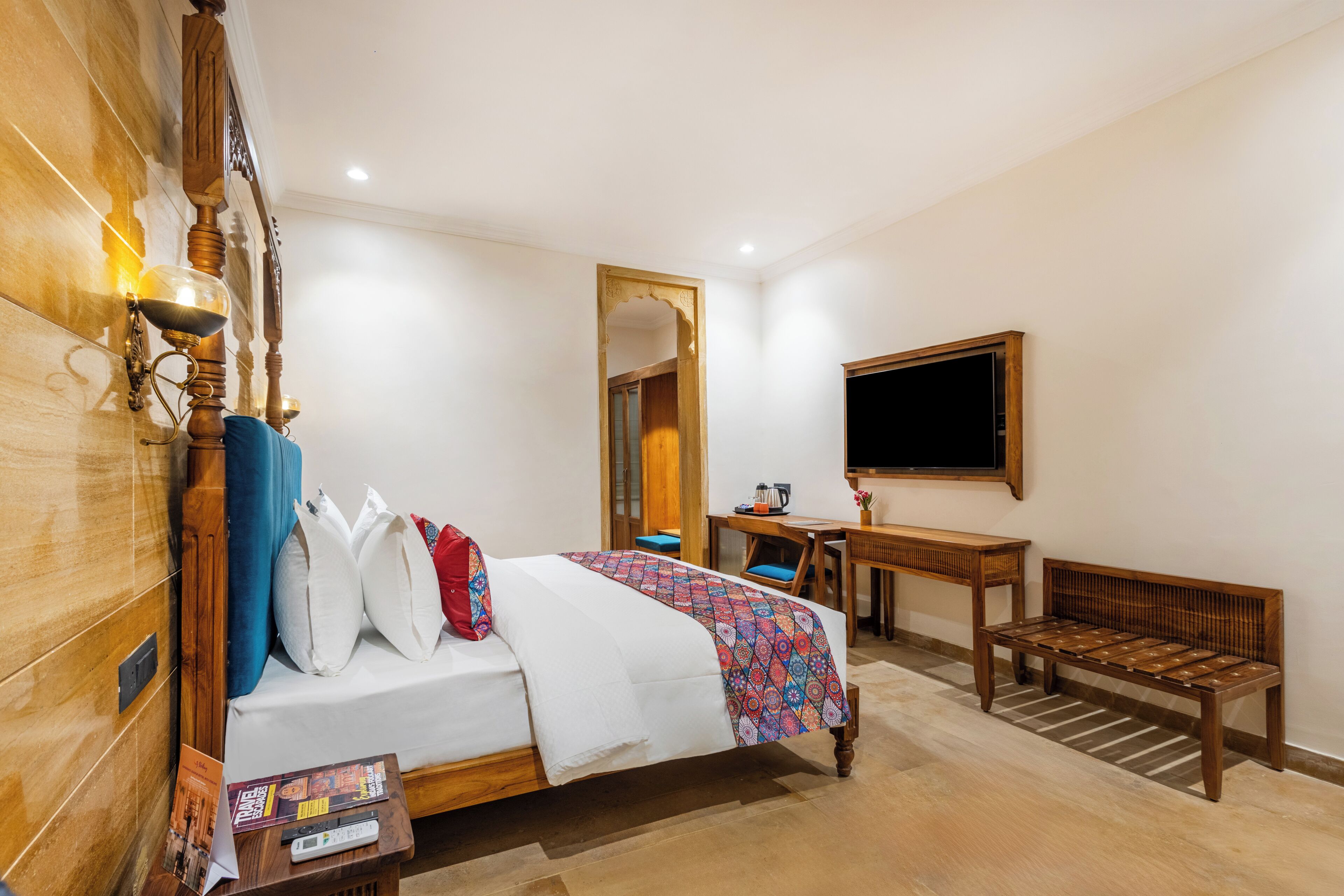 Une chambre d’hôtel avec un lit en bois, un bureau, un banc et un téléviseur fixé au mur.