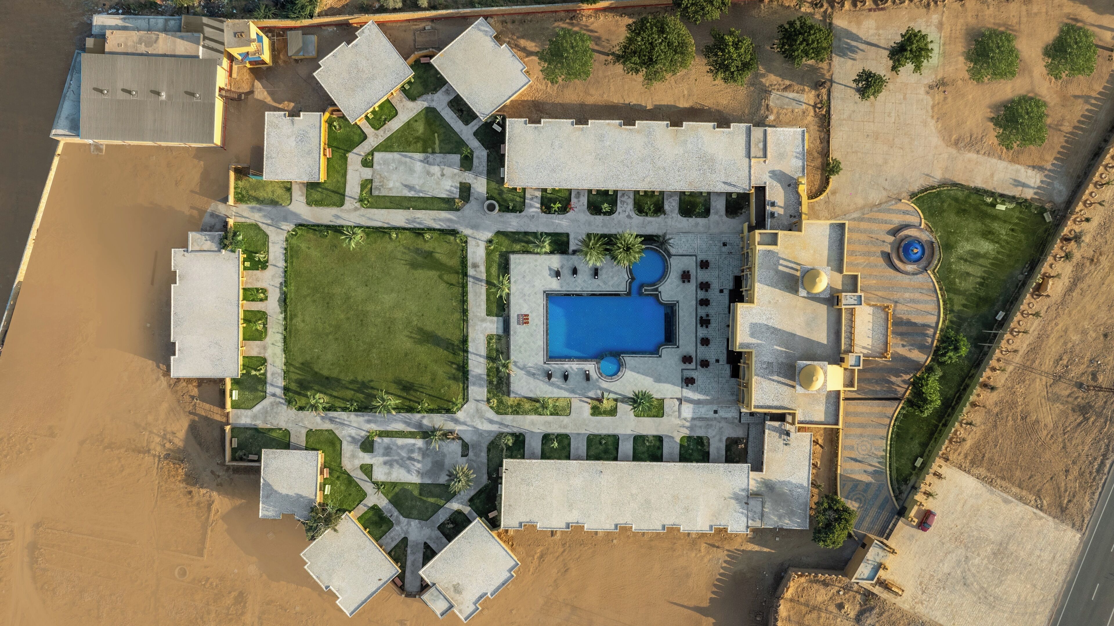 An aerial view of a resort with a central pool, multiple guest rooms, and landscaped areas.