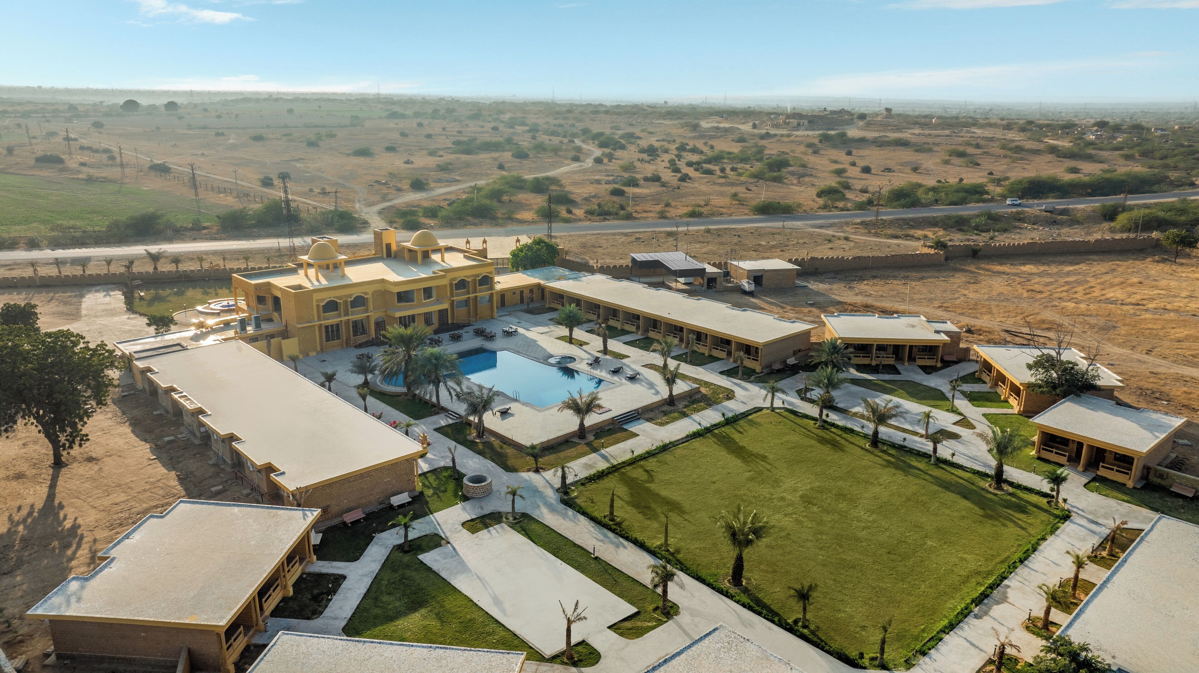 A large hotel with multiple buildings, a swimming pool, and a well-maintained lawn.