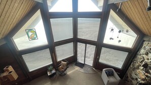 A cozy room with a stone fireplace, large windows, and a wooden ceiling.
