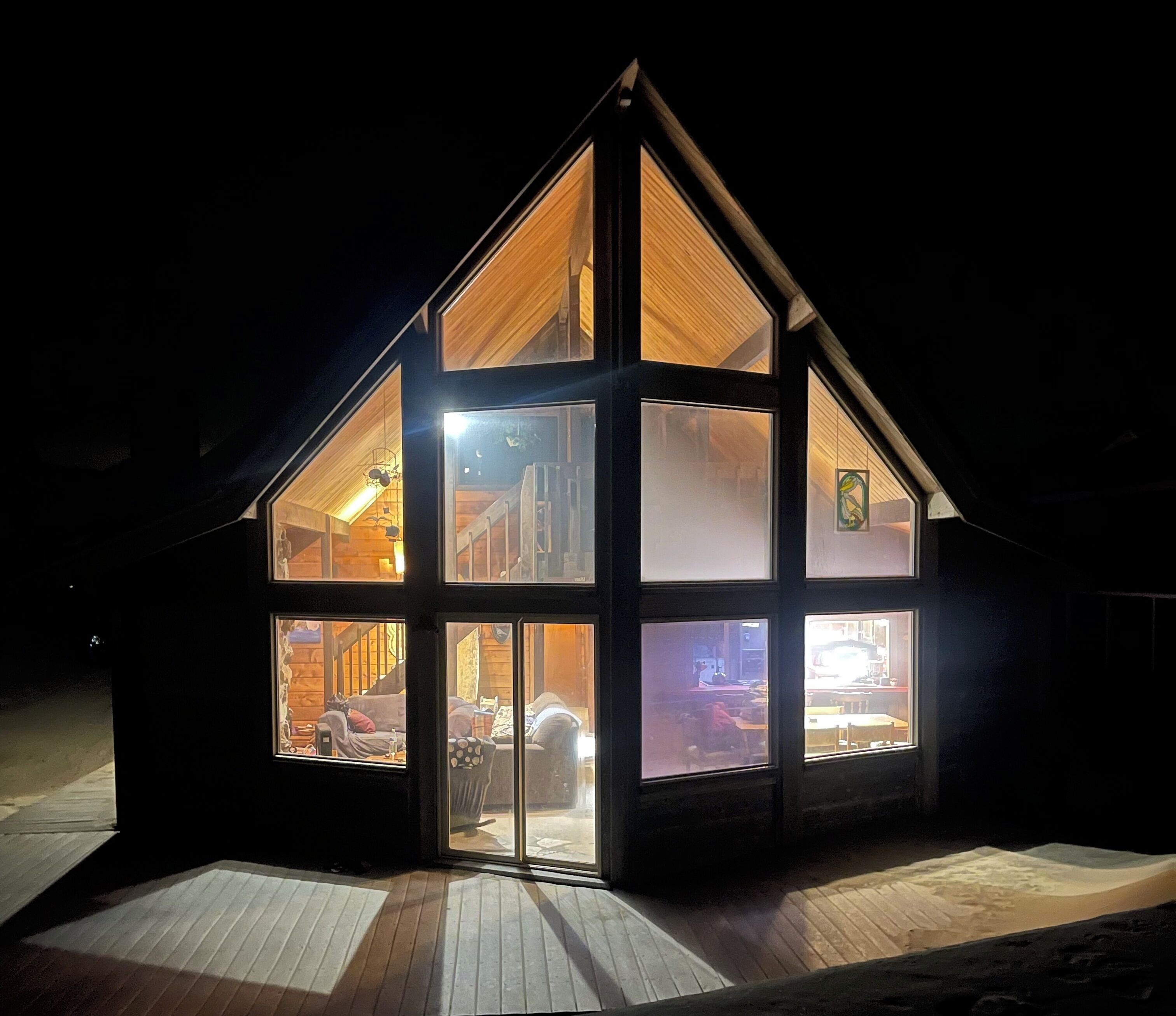 A modern, multi-level wooden house with large windows, a sloped roof, and a wooden deck.