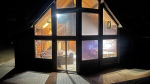 A modern, multi-level wooden house with large windows, a sloped roof, and a wooden deck.