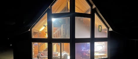 A modern, multi-level wooden house with large windows, a sloped roof, and a wooden deck.