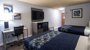 A hotel room with a bed, desk, chair, TV, and artwork on the walls.