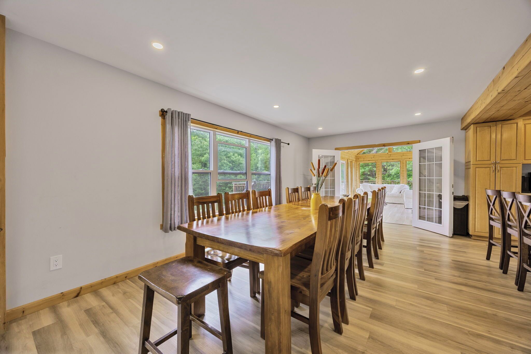 Une salle à manger spacieuse avec une longue table et des chaises en bois, de grandes fenêtres avec des rideaux et une vue sur la verdure environnante.