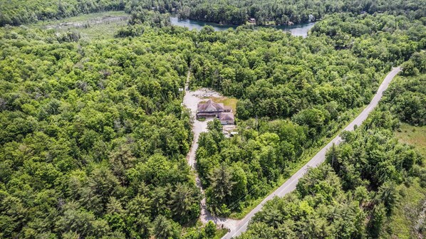 Une vue aérienne d’une zone boisée, avec une seule maison entourée d’arbres denses et une route sinueuse.