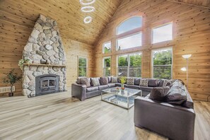 A spacious living room with a stone fireplace, large windows, and a modern sofa set. - Waterfront 10BR Retreat on 7 Private Acres | Green River Villa | Sleeps 28–30 (Washago)