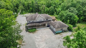 Une maison à deux étages dotée d’un porche abrité et d’un garage séparé, entourée d’une forêt dense.