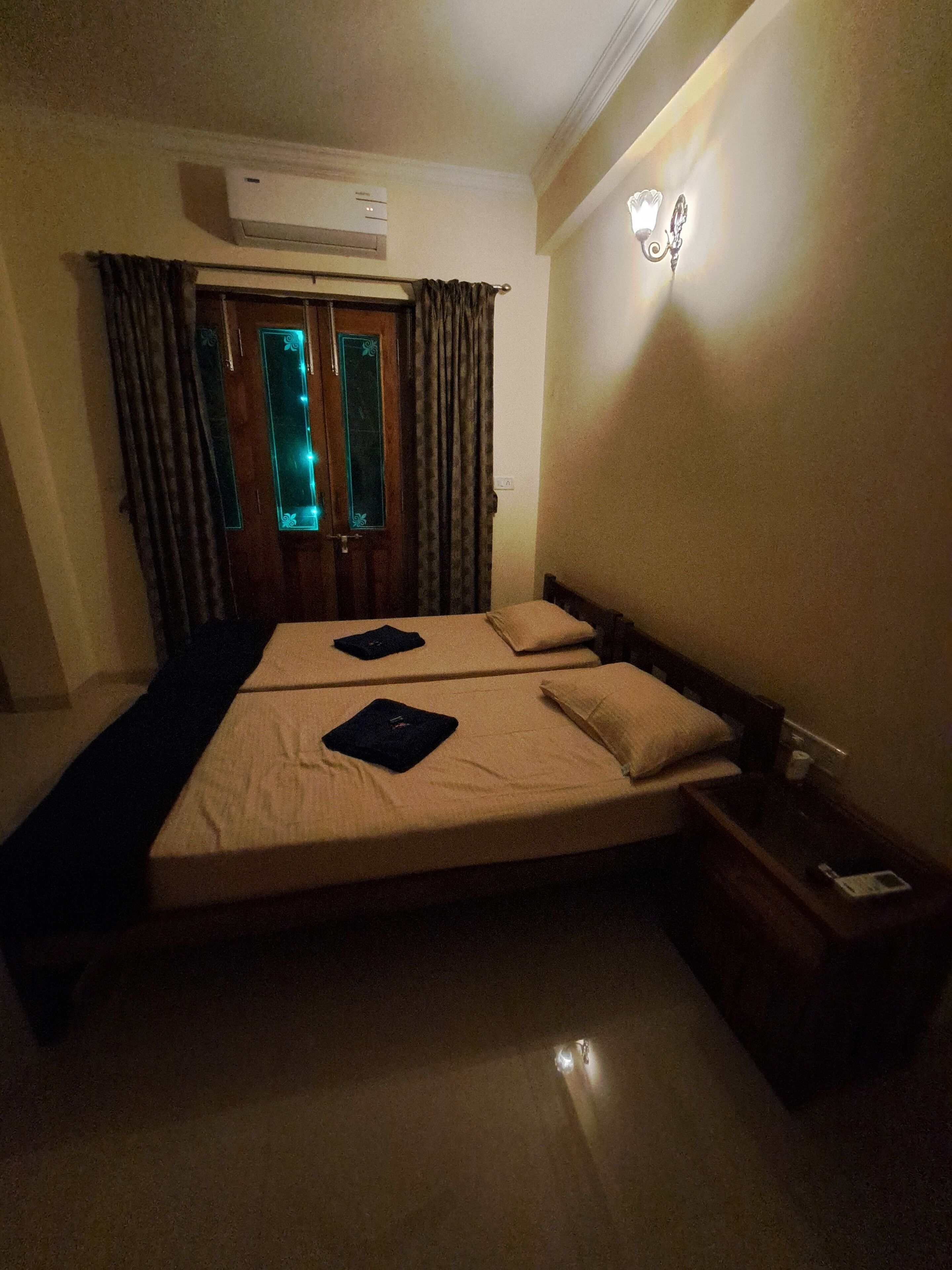 Habitación de hotel con dos camas, una mesita de noche, un equipo de aire acondicionado y una ventana con cortinas.