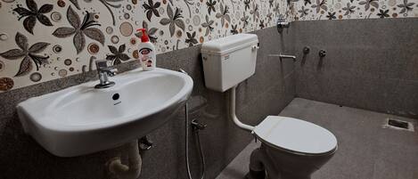 Un baño con lavamanos, inodoro y ducha blancos. Las paredes están decoradas con motivos florales.