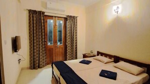 A hotel room with a bed, a ceiling fan, a door with curtains, and a wall-mounted light fixture. - Dsouzas Guest House (Bardez)