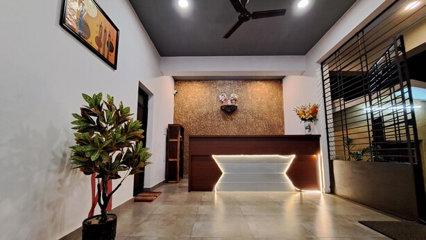 A reception area with a modern design, featuring a ceiling fan, a reception desk with integrated lighting, a decorative wall, and a potted plant. - Dsouzas Guest House (Bardez)
