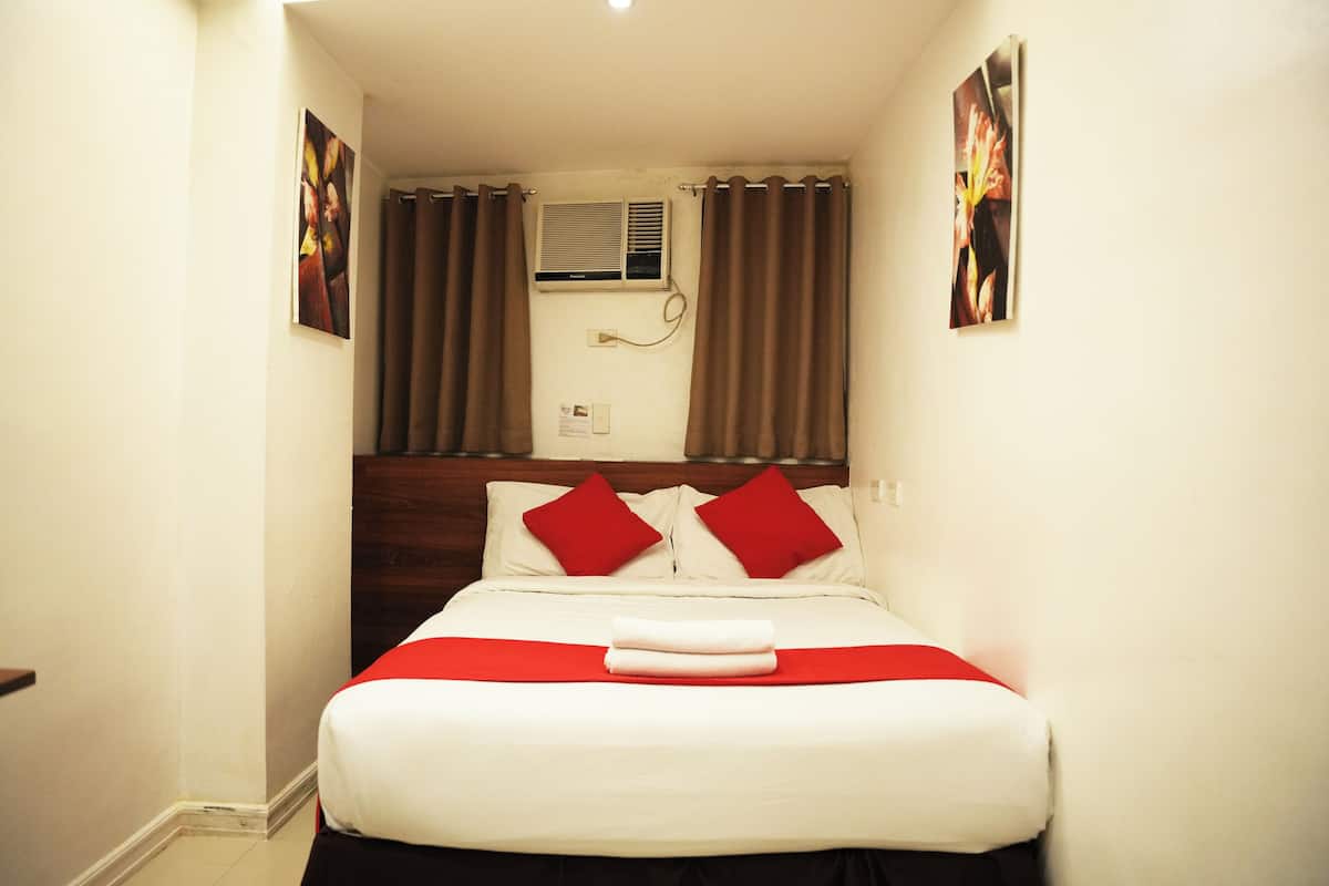 Quarto de hotel com uma cama, almofadas vermelhas, edredão branco e manta vermelha.