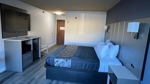 Une chambre d’hôtel moderne dotée d’un grand lit, d’un téléviseur à écran plat, d’un bureau avec des tiroirs et d’une porte donnant sur une autre pièce.