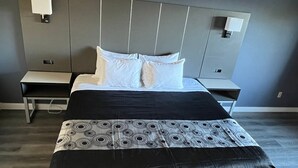 Une chambre d’hôtel moderne dot ée d’un grand lit, d’une table de chevet, d’une petite table et d’une tête de lit avec un éclairage intégré.