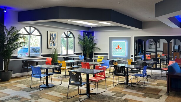 Un espace de restauration intérieur moderne, doté de nombreuses tables et chaises, de grandes fenêtres et de plantes d’intérieur.