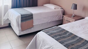 A hotel room with two beds, a nightstand with a lamp, and a window with curtains.