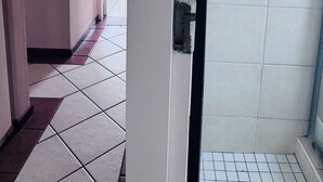 A bathroom with a shower, tiled floor, and a door leading to a hallway.